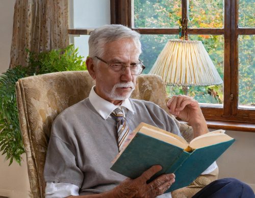 um idoso sentado em uma cadeira confortável, lendo um livro com a expressão seria e pensativa